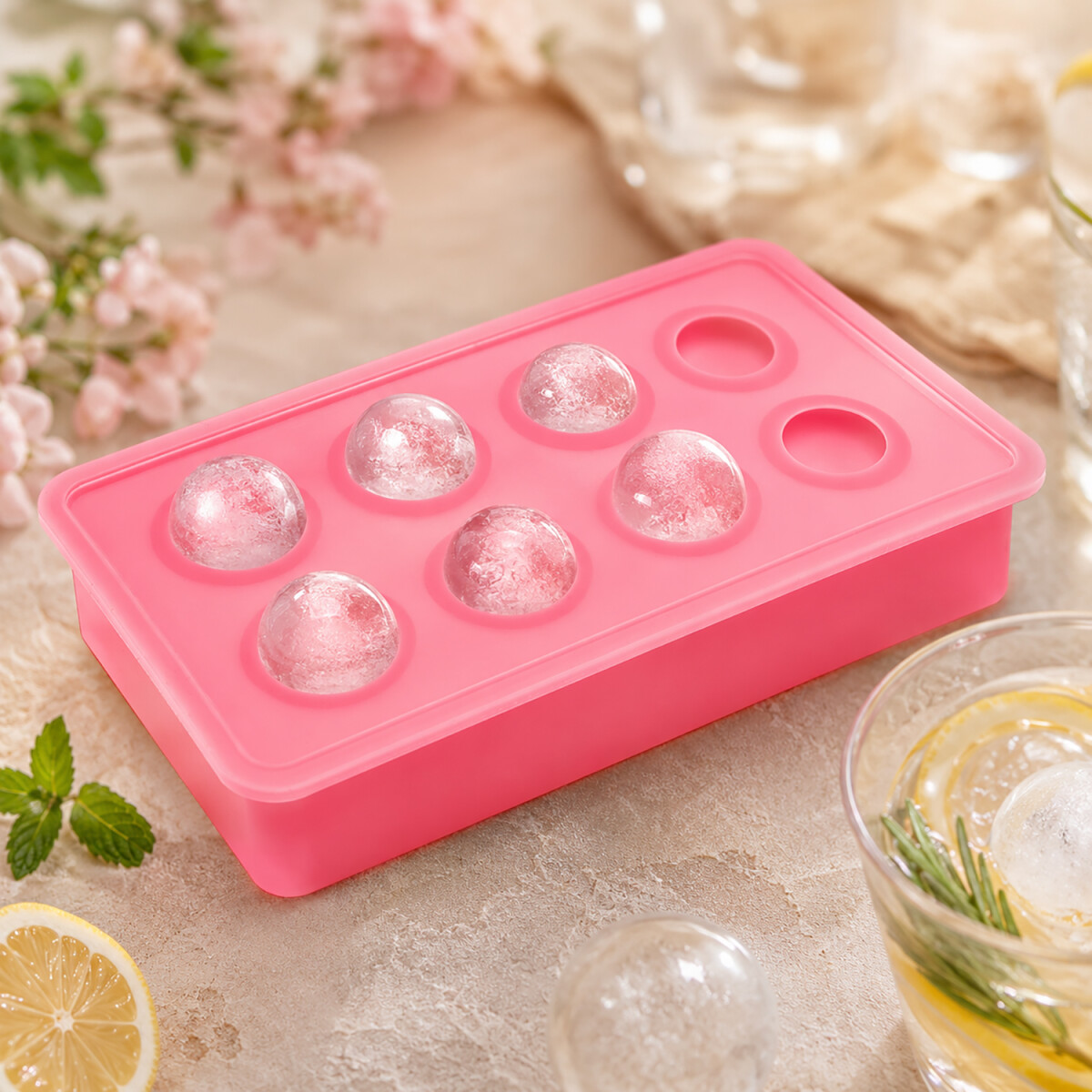 Sommerlicher Cocktail mit runden Eiskugeln in der Hand bei Abendsonne auf einer Terrasse mit Limette, Minze und warmem Sonnenlicht